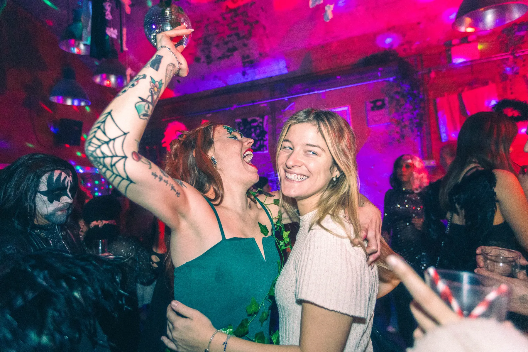 Two friends laughing under the disco ball at a Love Shack Halloween party in The Bunker