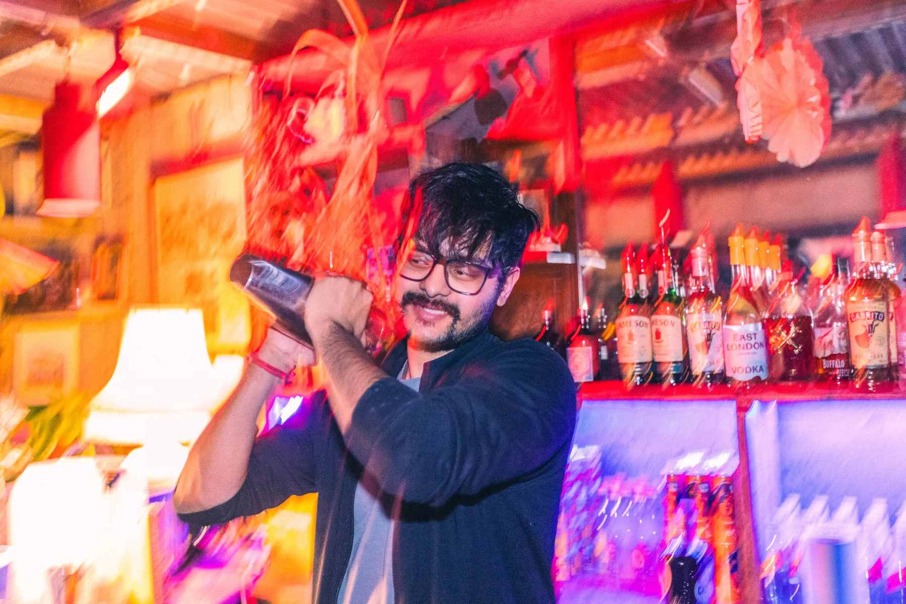 A bartender shaking a cocktail under red light at Love Shack