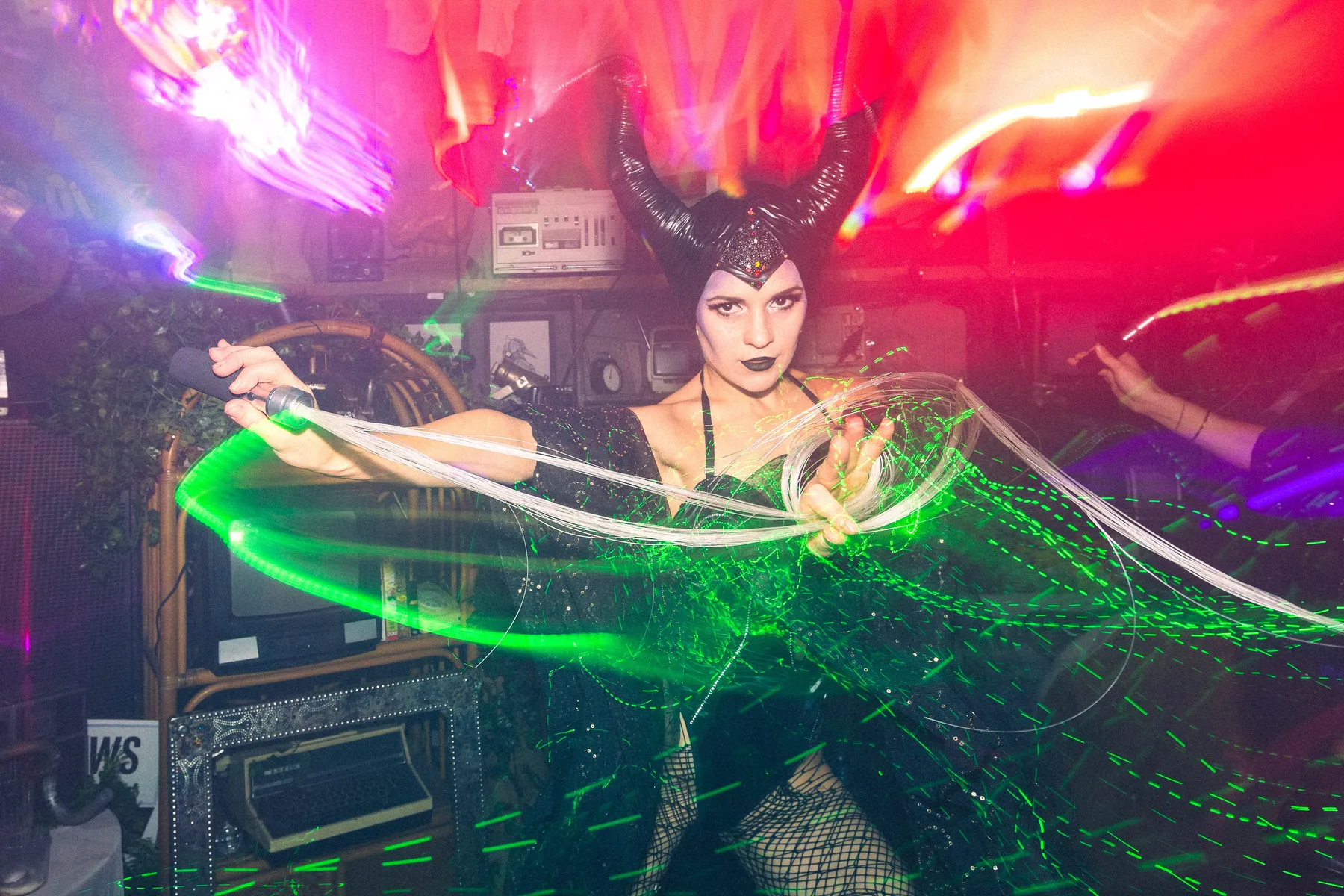 A performer in Maleficent horns lit by green lasers at a Love Shack Halloween party